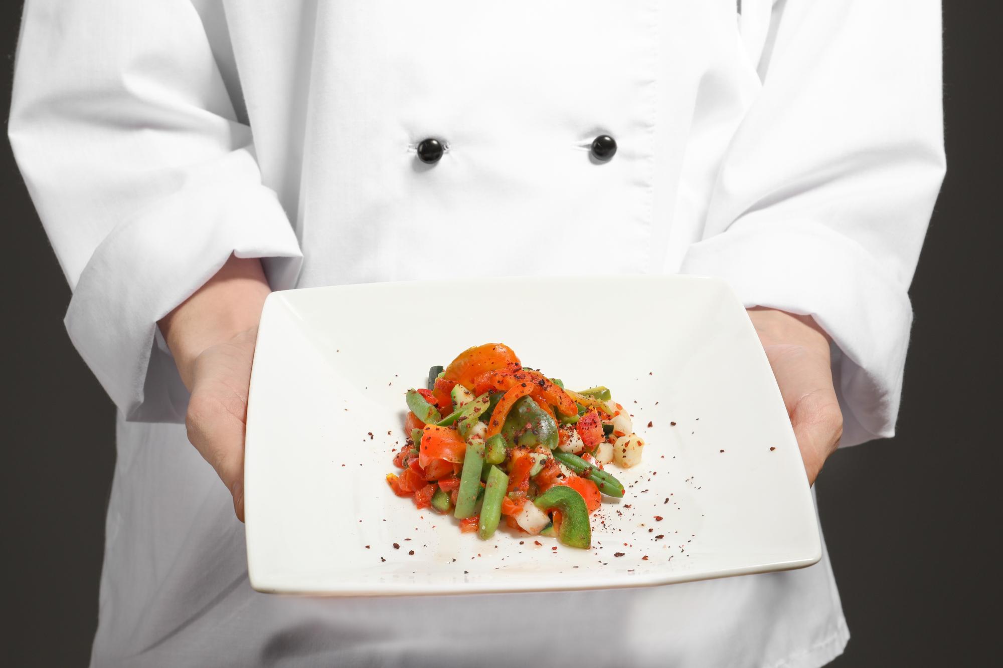 Chef instructor demonstrating a plated dish in a modern kitchen